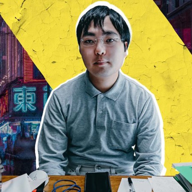 y-Kollektiv: ein junger Mensch mit Brille sitzt vor einem Tisch auf dem Handy, Mouse und Papiere liegen im Hintergrund gelb und ein asiatisches Schriftzeichen
